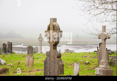 Un groupe de vieilles pierres tombales celtiques traverse un cimetière au bord de l'eau dans les zones rurales de l'Irlande. Banque D'Images