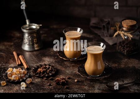 Thé ou café avec lait et épices en verre Armudu avec grains de café et sucre sur fond sombre. Banque D'Images