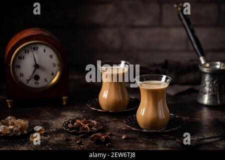 Thé ou café avec lait et épices en verre Armudu avec grains de café et sucre sur fond sombre. Banque D'Images