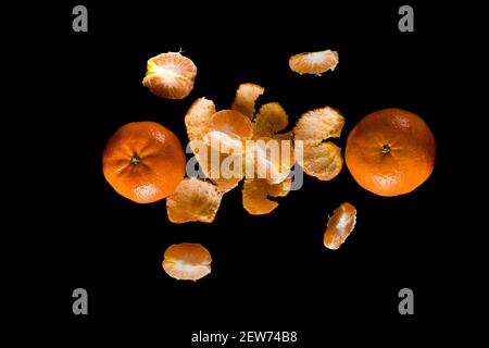 Fruit mûr de la mandarine d'agrumes, entier et en tranches et avec des morceaux de pelure sur un fond noir Banque D'Images