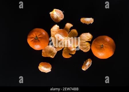 Fruit mûr de la mandarine d'agrumes, entier et en tranches et avec des morceaux de pelure sur un fond noir Banque D'Images