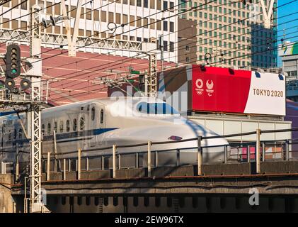 tokyo, japon - mars 02 2021: Gros plan sur une série Shinkansen bullet train 700 passant à la gare Yurakucho en face des panneaux publicitaires de Tokyo 2020 O Banque D'Images