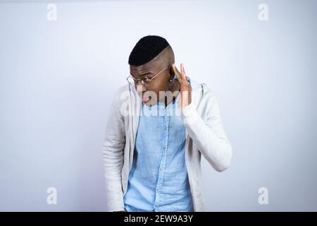 Jeune homme afro-américain élégant portant des vêtements décontractés surpris passer la main sur l'oreille pour écouter une rumeur ou des potins Banque D'Images