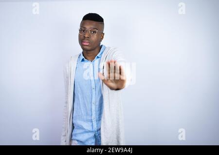 Jeune homme afro-américain élégant portant des vêtements décontractés sérieux et faisant cesser de chanter avec la paume de la main. Banque D'Images