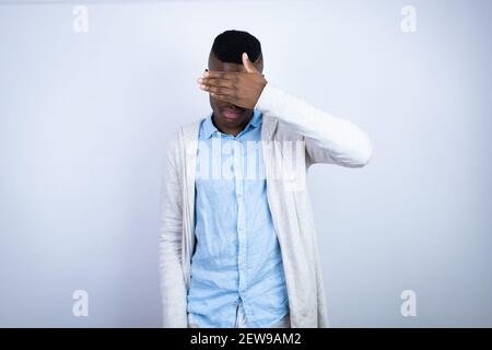 Jeune homme afro-américain élégant portant des vêtements décontractés sérieux et couvrant ses yeux avec sa main Banque D'Images