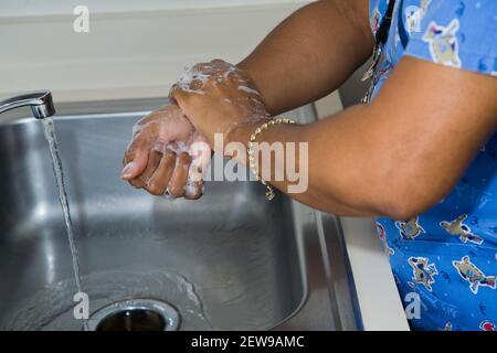 Une infirmière afro-américaine se lavant les mains dans un acier inoxydable lavabo dans un hôpital ou une clinique médicale Banque D'Images