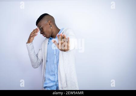 Jeune homme afro-américain élégant portant des vêtements décontractés couvrant les yeux avec les mains et faisant un geste d'arrêt avec l'expression de la tristesse et de la peur. Embarrassé un Banque D'Images