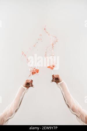 Deux mains en blouse blanche clinking verres de vin rose faisant des éclaboussures sur fond blanc de mur. Boutique de vins, dégustation de vins, bar, carte des vins, concept Spring Mood Banque D'Images