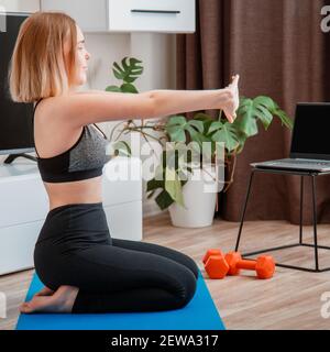 Femme sportive utilisant des haltères faisant du fitness à la maison via un ordinateur portable par appel vidéo en ligne à distance. Jeune femme perdant du poids par l'entraînement en ligne à distance de gym. Carré Banque D'Images