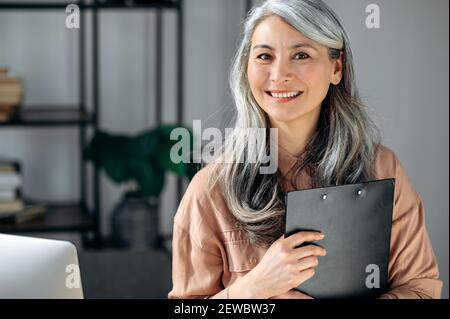 Portrait en gros plan d'une femme, d'une femme d'affaires ou d'un coach à cheveux gris, satisfaite et satisfaite, debout au bureau, souriant dans l'appareil photo Banque D'Images