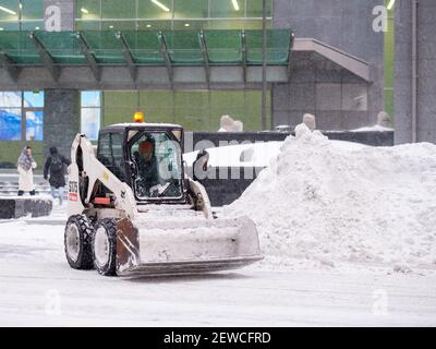 Moscou. Russie. 12 février 2021. Une petite pelle hydraulique avec un godet élimine la neige d'une route dans une rue urbaine lors d'une forte chute de neige. Hiver da Banque D'Images