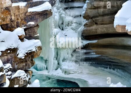 Une image horizontale de l'Athabasca tombe en hiver avec de la glace gelée accrochée aux parois du canyon rocheux dans le parc national Jasper, en Alberta, au Canada. Banque D'Images