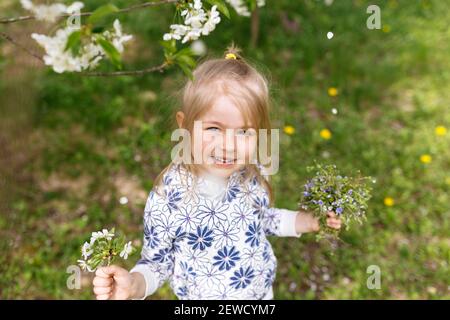 Petite fille avec fleurs de printemps sur pelouse verte dans le jardin. Photo de haute qualité Banque D'Images