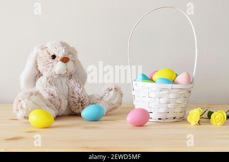Lapin jouet de Pâques, œufs colorés avec panier et petites fleurs sur table en bois avec fond blanc et espace de copie. Banque D'Images