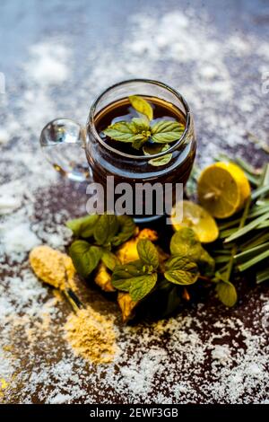 Injection de kada ayurvédique ou boisson d'immunité sur une surface brune composée de citronnelle, citron, feuilles de menthe, soonth ou poudre de gingembre séchée. Banque D'Images