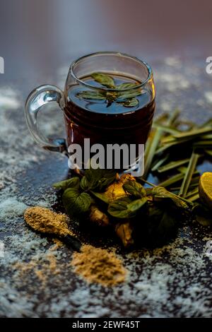 Injection de kada ayurvédique ou boisson d'immunité sur une surface brune composée de citronnelle, citron, feuilles de menthe, soonth ou poudre de gingembre séchée. Banque D'Images