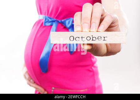 Femme enceinte en robe rose avec ruban bleu montrant le mot octobre écrit sur cube en bois. S'attendre au nouveau-né et à l'expansion de la famille Banque D'Images