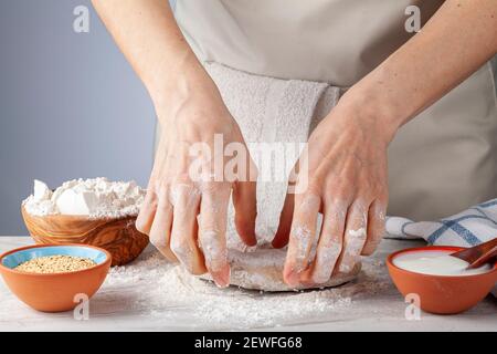 Préparation de base de pain plat, de pide ou de pizza dans la cuisine. Une femme chef pétrit et aplatit toute la pâte organique de grain i Banque D'Images