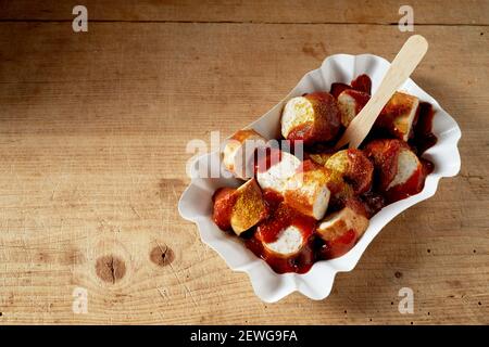 Grand angle de tranches de saucisse de porc douces appétissantes recouvertes de sauce tomate et curry sec dans un récipient jetable Banque D'Images