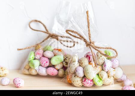 Oeufs de Pâques, bonbons en glaçure colorée dans des sacs transparents sur fond clair Banque D'Images