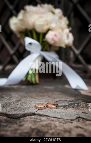 Anneaux d'or de mariage sur le fond du bouquet de la mariée avec roses et treillis métallique Banque D'Images