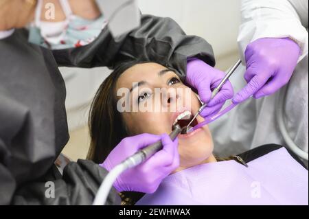 Une jeune femme visite la clinique de dentisterie pour un traitement dentaire professionnel. Femme dentiste se plie au-dessus du patient. Médecin tenant instrument outil pour voie orale
