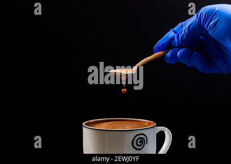 La main d'une personne portant un gant en latex tient Une cuillère à laquelle une goutte de Latte tombe.c'est photo au format horizontal prise sur fond noir Banque D'Images