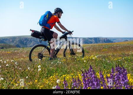 Le cycliste passe au printemps parmi les champs de fleurs et les collines. Un homme barbu fait du vélo à l'extérieur par une journée d'été Banque D'Images