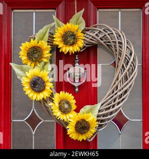 Une décoration de porte en forme de coeur de canne et de tournesol accrochée à une porte rouge vif et en verre avec un knocker argenté. Banque D'Images