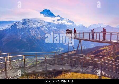 Grindelwald, Suisse - 10 octobre 2019: Les gens sur le ciel de la falaise marchent le pont en métal au premier sommet de la montagne des Alpes suisses, les sommets de neige rose coucher de soleil panora Banque D'Images