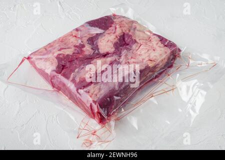 Viande pastrami emballée dans des sacs en plastique sous vide, sur fond de pierre blanche , avec espace de copie et espace pour le texte Banque D'Images