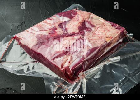 Viande pastrami emballée dans des sacs en plastique sous vide, sur fond de pierre noire Banque D'Images