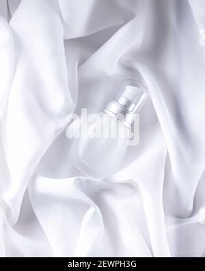 Bouteille de cosmétique blanche en soie douce. Concept esthétique et esthétique. Composition de couleurs minimale. Vue de dessus, plat, espace de copie Banque D'Images