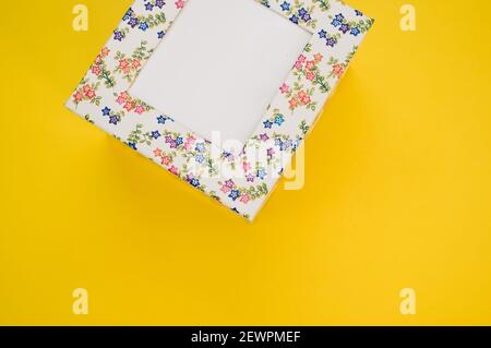 Vue de dessus d'une boîte en carton cubique avec fleur motifs isolés sur fond jaune Banque D'Images