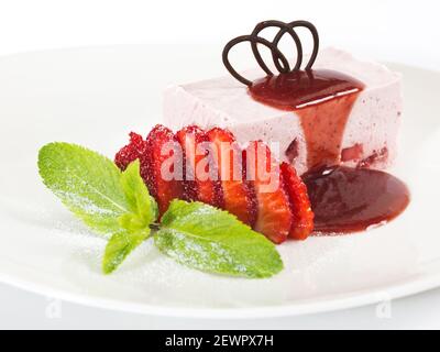 morceau de cheesecake à la fraise sur une assiette blanche servi avec frais fraises et garnies de sirop Banque D'Images