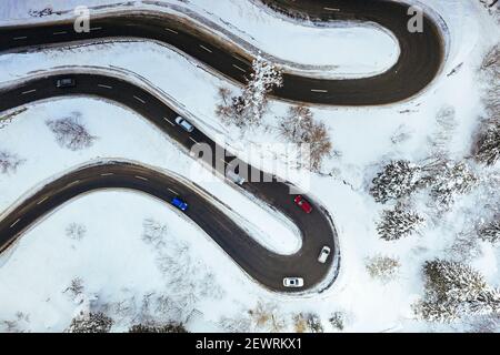 Vue aérienne des voitures roulant sur des virages de route enneigée de montagne en hiver, Suisse, Europe Banque D'Images