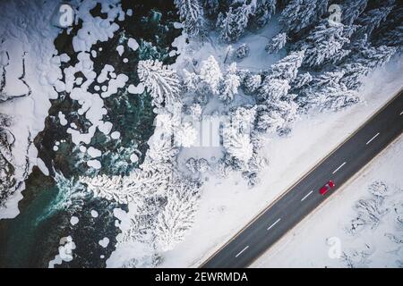 Voiture voyageant sur la route de montagne enneigée sur le côté de la rivière et des bois gelés, vue aérienne, Suisse, Europe Banque D'Images