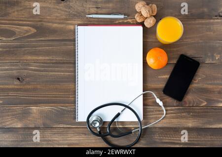 Vue de dessus du bureau d'un médecin. Ordinateur portable, stéthoscope et téléphone portable sur fond de bois sombre. Espace pour le texte. Banque D'Images