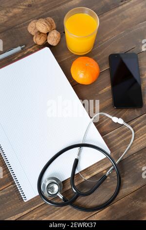 Vue de dessus du bureau d'un médecin. Ordinateur portable, stéthoscope et téléphone portable sur fond de bois sombre. Banque D'Images