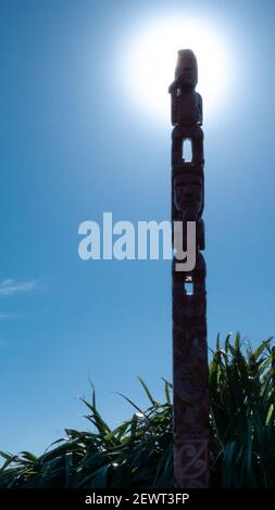 Totem maori traditionnel en bois avec soleil levant derrière lui et ciel bleu clair, Portrait réalisé au Mont Victoria, Wellington, Nouvelle-Zélande Banque D'Images