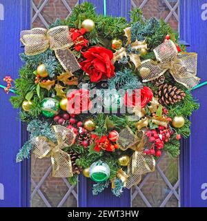 Gros plan de la porte avant de la maison bleue et de la couronne de Noël Avec des décorations de Noël y compris des boules de sapin cône ruban et Fleurs artificielles Angleterre Royaume-Uni Banque D'Images