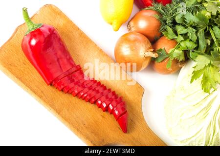 Poivron rouge haché sur panneau de bois avec d'autres légumes isolés sur un blanc. Banque D'Images