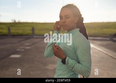 Femme afro-américaine se concentrant, portant des vêtements de sport s'exerçant dans le parc mettant des écouteurs dans