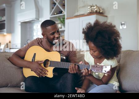 Homme afro-américain et sa fille assise sur un canapé joue de la guitare Banque D'Images