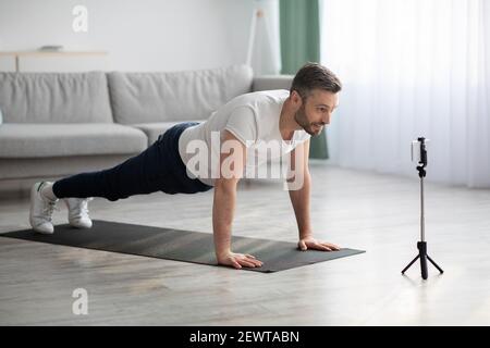 Entraînement sportif motivé sur tapis de fitness, diffusion avec smartphone Banque D'Images