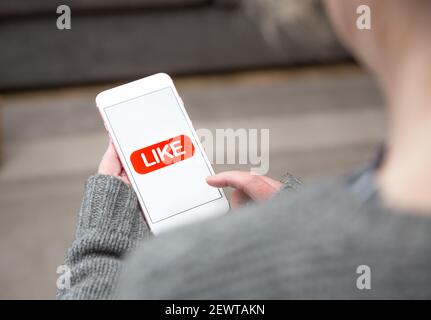 Une femme touchant une icône similaire sur l'écran tactile de son téléphone mobile dans un concept de médias sociaux Banque D'Images