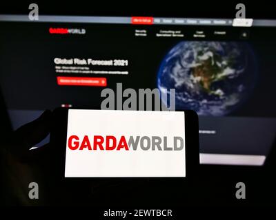 Personne tenant un smartphone portant le logo de la société canadienne de sécurité privée GardaWorld Corporation à l'écran devant le site Web. Mise au point sur l'affichage du téléphone. Banque D'Images