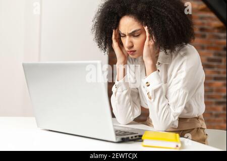 Une femme d'affaires ou une étudiante exténuée, entrepreneur de race mixte, a fermé les yeux touchant des temples massants souffrant de migraines sévères, une jeune femme ethnique fatiguée submergée de travail informatique Banque D'Images