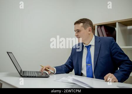 Jeune homme d'affaires travaillant à la maison avec un ordinateur portable et des papiers sur le bureau Banque D'Images