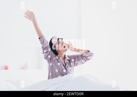 Photo de mignon drôle jeune femme vêtements de nuit lit bâillement ouverture de la bouche à l'intérieur de la pièce à la maison Banque D'Images